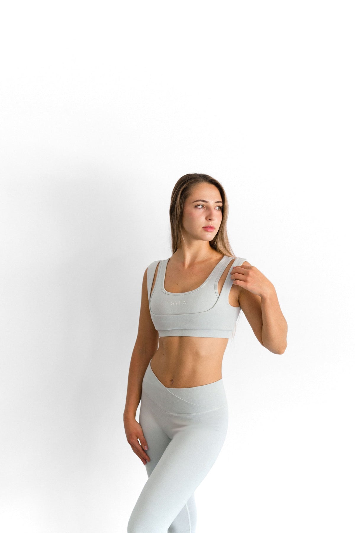 Model adjusting the strap of the sage SYLA Sculpt Bra, worn with matching Sculpt Leggings