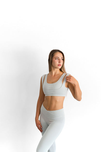 Model adjusting the strap of the sage SYLA Sculpt Bra, worn with matching Sculpt Leggings