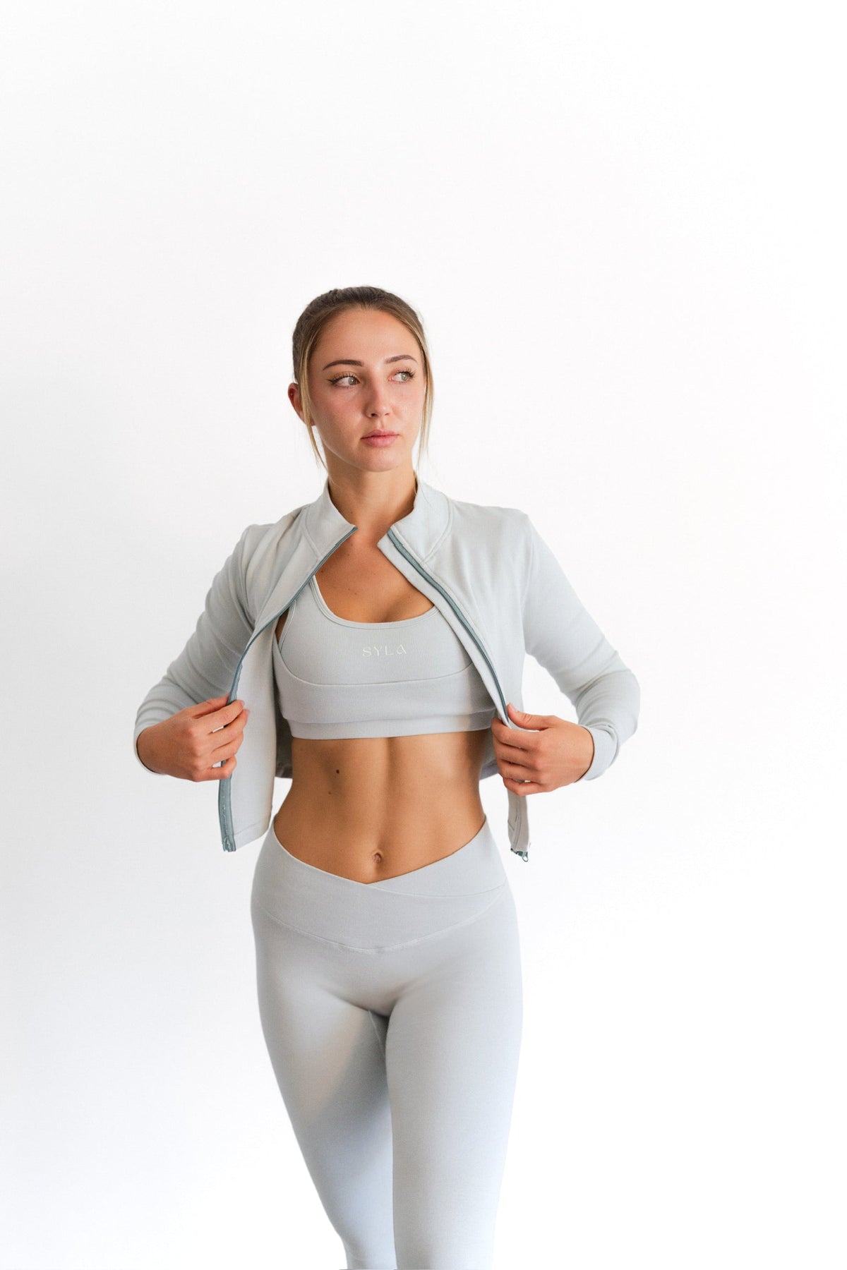 Model holding open the sage SYLA Sculpt Jacket, showing its cropped fit
