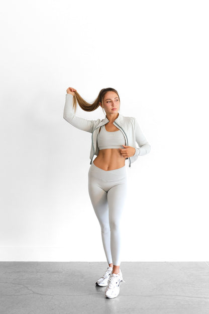 Full-length view of the sage SYLA Sculpt Jacket worn open over matching bra and leggings