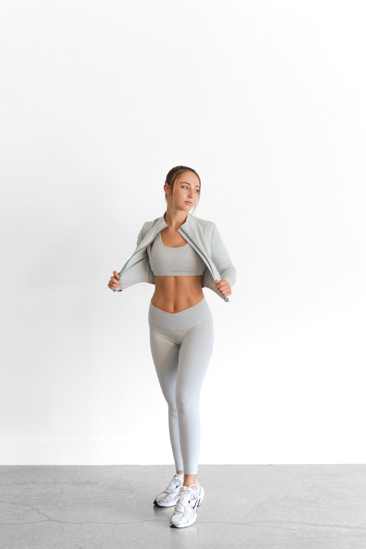The sage SYLA Sculpt Jacket worn open, showing its cropped length and mock neck collar