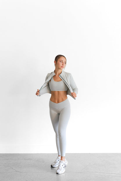 The sage SYLA Sculpt Jacket worn open, showing its cropped length and mock neck collar