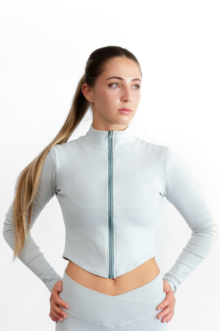 Close front view of the sage SYLA Sculpt Jacket, showing the full-length zip and mock neck collar