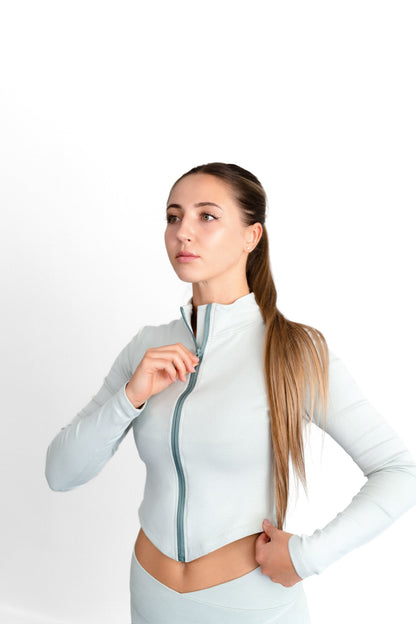 Model zipping the sage SYLA Sculpt Jacket, showing the contrast zip tape