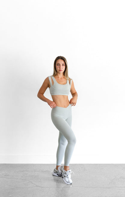 The sage SYLA Sculpt Bra worn with matching high-waist leggings, full-length front view