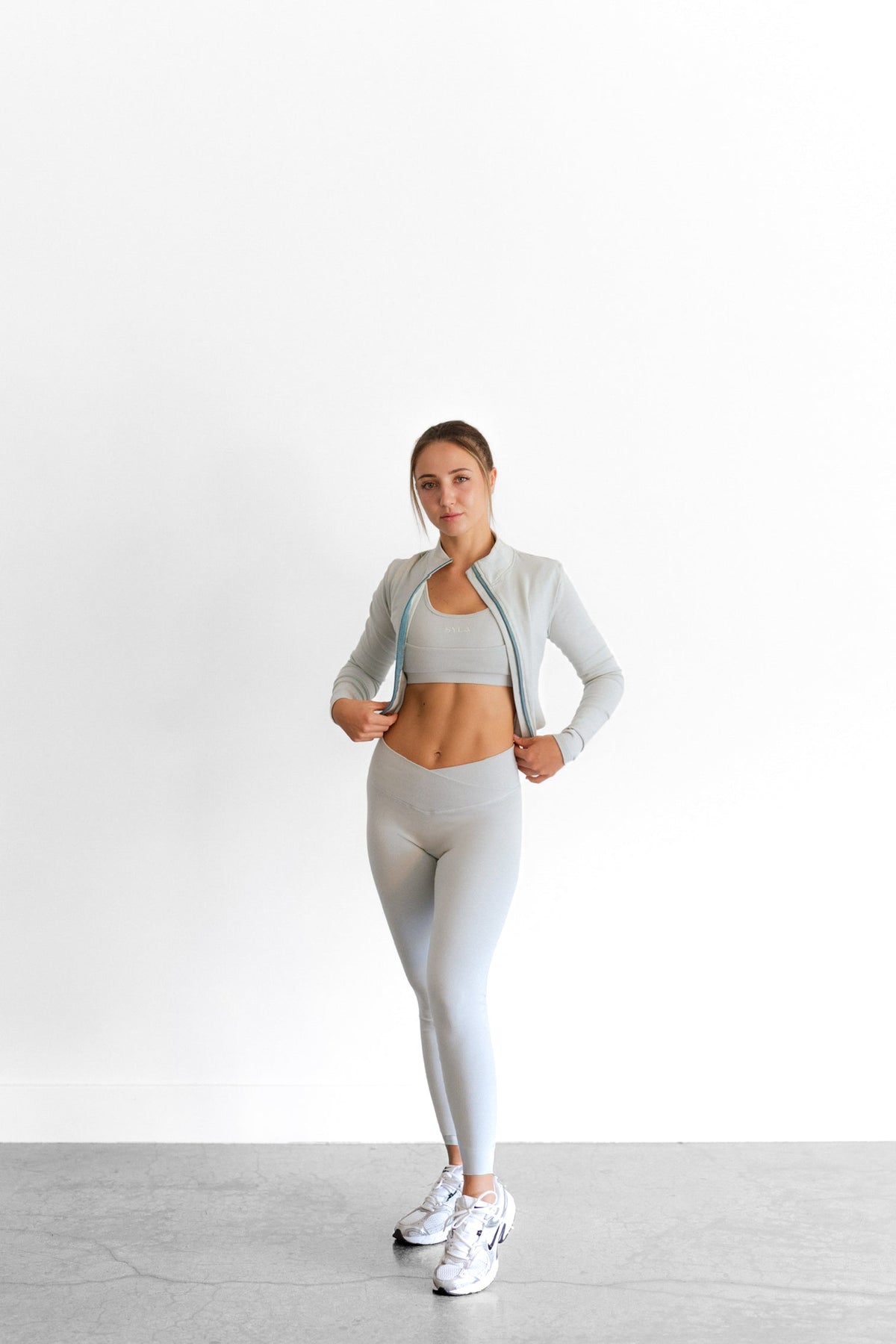 Full-length view of the sage SYLA Sculpt Set, cropped zip jacket layered over the Sculpt Bra and Leggings